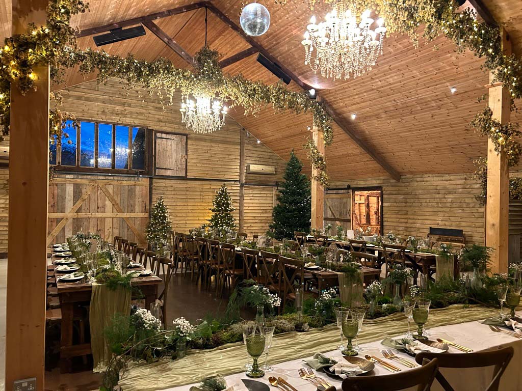High Billinghurst Farm Surrey barn wedding venue decorated for a winter wedding with chandeliers, banquet tables, greenery, and Christmas trees